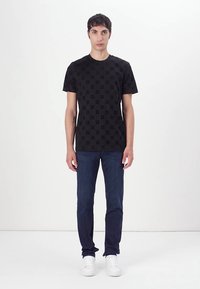 T-shirt en coton noir avec un motif subtil. Manches courtes et col rond, associé à un jean en denim foncé et des baskets blanches.
