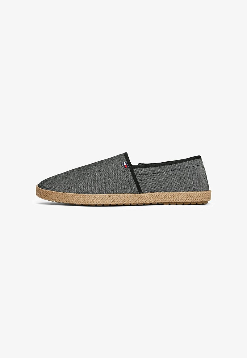 Espadrille grise en toile, sans lacets, avec un bout pointu, des accents en tissu noir et une semelle tissée en jute. Possède une petite étiquette logo sur le côté.