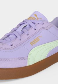 Βιολετί αθλητικό παπούτσι Puma με ανοιχτό πράσινο ρίγα, λαστιχένια σόλα και χρυσό λογότυπο Puma στο πλάι και στη γλώσσα, κοντινή λήψη στα κορδόνια και το επάνω μέρος.