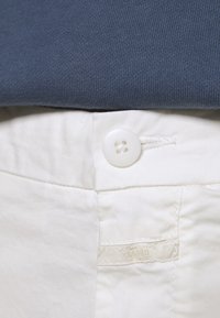 Vita bomullsbyxor med knappstängning framtill och en prydlig tygetikett. Den mörkblå skjortan är gjord av elastiskt ribbat material.