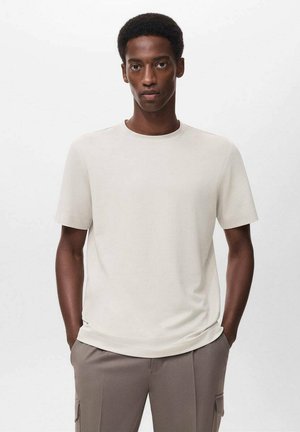 Camiseta de manga corta y cuello redondo en tejido de color beige claro con una textura suave. Combinada con pantalones sueltos en tono topo.