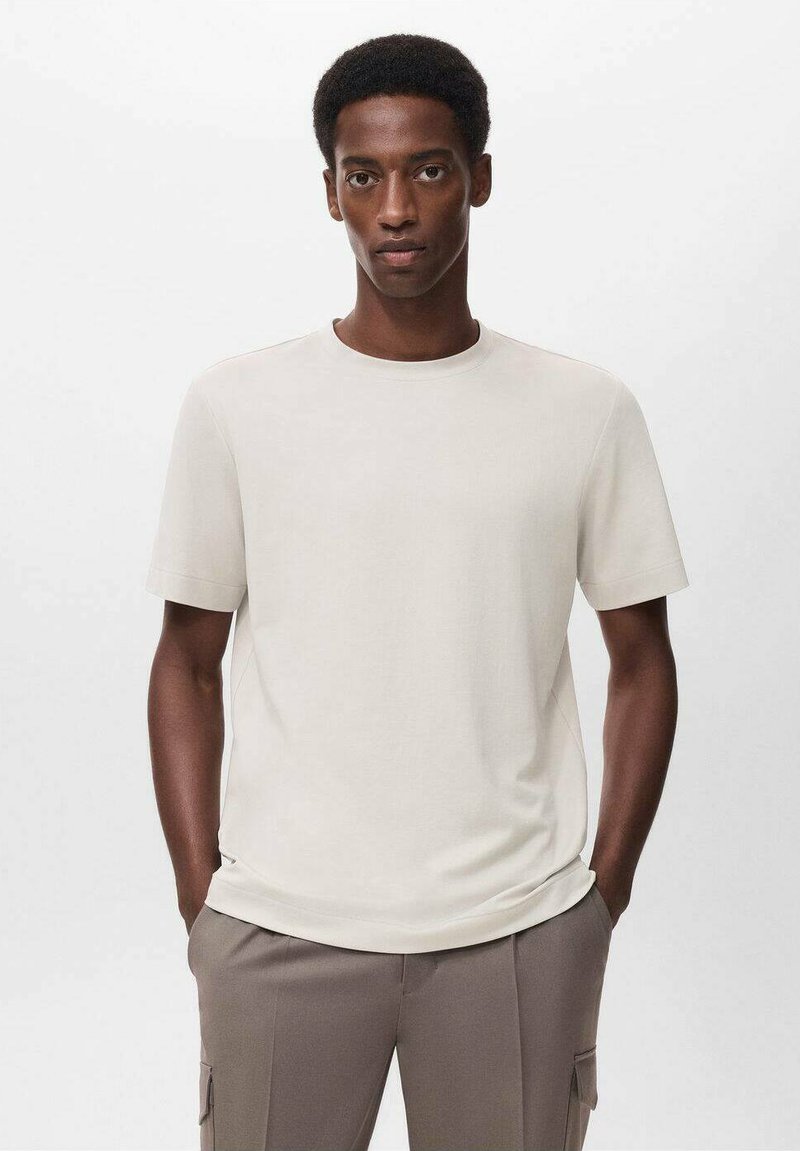 T-shirt a maniche corte e collo rotondo in tessuto beige chiaro con una texture liscia. Abbinato a pantaloni larghi color taupe.