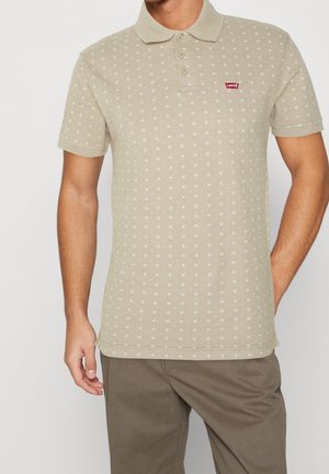 Polo beige en coton, avec un motif étoile, une patte à trois boutons et le logo Levi's sur la poitrine. Manches courtes et texture douce.
