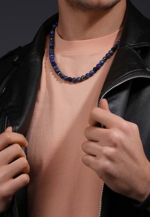 Beaded necklace with blue, black, and white stones; worn over a light pink shirt with a black leather jacket partially visible.