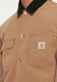 Beige bomulds skjorte med en sort velourkrave, gyldne trykknapper og to brystlommer med et mærke patch.
