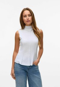Witte mouwloze top met een hoge halslijn, textuurstof en paneel details, gecombineerd met lichtblauwe wijde jeans.