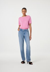 Roze trui met korte mouwen en een ronde hals, met schouderaccenten, gecombineerd met lichtblauwe rechte jeans en zwarte haksandalen.