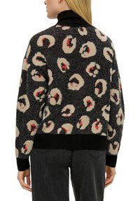 Zwart sweater met een fuzzy luipaardprint in beige en rode accenten. Heeft een zwarte geribbelde halslijn en manchetten, en een ontspannen pasvorm.