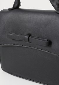 Bolso de mano de cuero sintético negro con una textura suave, que presenta un lazo plano y detalles cosidos a lo largo del borde.