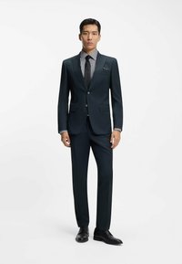 Donkergroen pak met een strak ontwerp, voorzien van een reverskraag met inkeping, zilveren knopen en een gestreept overhemd. Gecombineerd met zwarte leren schoenen.