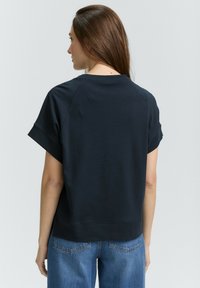 Haut noir à manches courtes avec une coupe décontractée, col rond et ourlet côtelé. Assorti à un jean en denim bleu, mettant en avant un style décontracté.