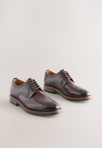 Scarpe eleganti in pelle marrone con design classico brogue, caratterizzate da dettagli traforati, punta tonda e tacco a blocco.
