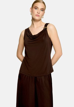 Femme portant un haut sans manches marron foncé avec un col drapé et une boucle dorée sur l'épaule gauche, associé à un pantalon large assorti.
