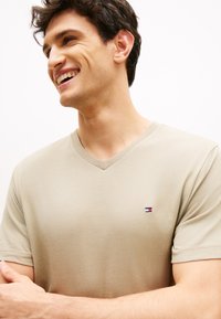 Μπεζ T-shirt με V λαιμόκοψη από απαλή ύφανση, με μικρή διακριτική λογότυπο με κόκκινες, λευκές και μπλε ρίγες στο αριστερό στήθος.