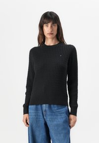 Pull en maille noire avec un motif texturé, encolure ronde et poignets côtelés. Assorti à un jean en denim bleu ample.