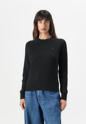 Svart strikket genser med teksturert mønster, rund hals og ribbede mansjetter. Kombinert med vide blå denimjeans.
