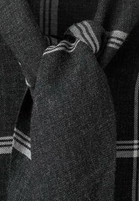 Šal u crno-sivoj kariranoj tkanini teksturiranog izgleda, s čvorom i prugastim detaljima na rubovima.