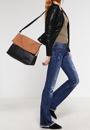 Musta nahkalaukku, jossa on vaaleanruskea mokkanahkainen läppä, olkahihna ja vetoketjusuljin. Malli käyttää tummansinisiä liehuvia farkkuja ja mustaa nahkatakkia.