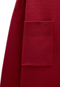 Czerwona dziana odzież z detalem kieszeni w prążki. Tkanina wydaje się miękka o gładkiej fakturze i jednolitym kolorze na całej powierzchni.