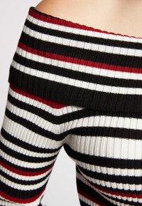 Czarno-biało-czerwony prążkowany top z odkrytymi ramionami, z teksturą prążkowaną i szerokim dekoltem. Paski mają różną szerokość.
