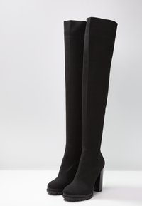 Botas negras hasta la rodilla con un tejido texturizado, tacón alto bloque y un acabado suave. Presenta una silueta ajustada y suela de goma.