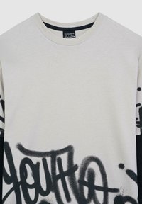 Kremowa koszulka z krótkim rękawem, ozdobiona czarnym nadrukiem w stylu graffiti z napisem "MŁODZIEŻ". Okrągły dekolt, wykonana z miękkiego materiału bawełnianego.