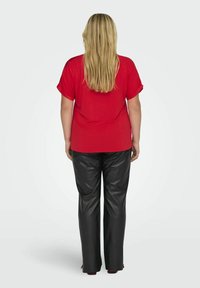 Röd kortärmad skjorta i kombination med svarta byxor i konstläder med vida ben. Modellen visad bakifrån, med hår som faller ner förbi axlarna.