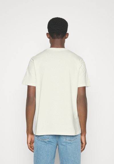 T-shirt de algodão cinza claro com mangas curtas, decote redondo e bainha reta, vestida com jeans de denim azul.