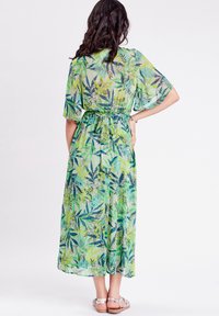 Robe maxi verte transparente avec un motif floral, manches courtes et une ceinture à nouer à la taille. Présente un design fluide et une longueur aux chevilles.