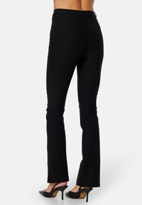 Zwarte flare pants met een gladde textuur, hoge taille en achterzakken. Gepaarde met zwarte hoge hakken met een spitse neus.