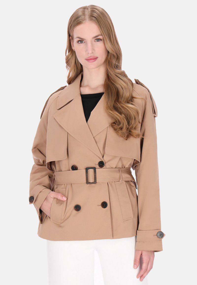 Beige trenchcoat med dobbeltradet design, store revers og bælte i taljen. Har knapdetaljer og forlommer.