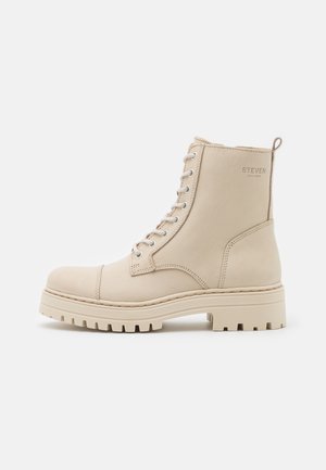 Beige snørestøvle med tyk, rillede såler og "STEVEN New York" trykt nær toppen på ydersiden.