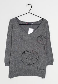 Gray knit sweater with a V-neck, three-quarter sleeves, floral cutout design, and a side pocket. Features a hanging tag and rounded hem.