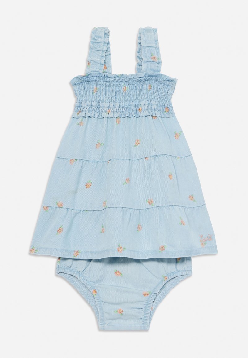 Svijetloplava pamučna haljina s volanima na naramenicama, smockanim korzetom i slojevitom suknjom koja ima male cvjetne uzorke. Uključuje pričvršćene gaćice.