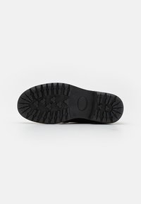 Suela de bota de goma negra con profundas ranuras para tracción, forma redondeada y surcos flexibles para mayor flexibilidad. Diseño limpio, sin acentos visibles.