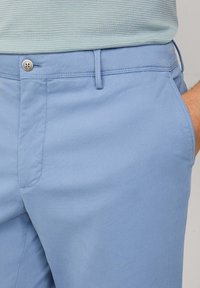 Light blue chinos with a smooth texture, featuring a button closure, side pockets, and a tailored fit.