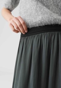 Gonna plissettata grigio scuro con una cintura elastica nera e testurizzata. Il tessuto ha un aspetto morbido e fluido, messo in risalto da delicate pieghe.