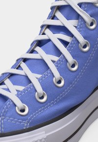 Κοντινό πλάνο μπλε πάνινα παπούτσια με λευκά κορδόνια περασμένα από μεταλλικά ρυθμιστικά και λευκή λαστιχένια σόλα με μαύρη ρίγα.