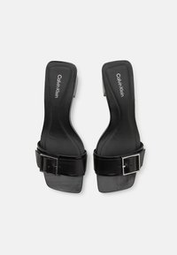 Sandales noires à talons avec une large sangle, bout carré et une boucle réglable. Elles disposent d'un cuir lisse et d'une semelle intérieure rembourrée.