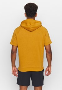 Felpa con maniche corte di colore giallo senape, realizzata in tessuto morbido. Presenta un cappuccio con coulisse, maniche raglan e una vestibilità comoda.