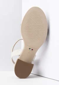 Sandal con tacco bianco con suola beige. Presenta una texture embossata, cinturino alla caviglia e etichetta del marchio. Taglia 37.