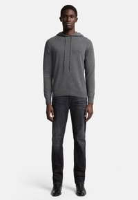 Grau Hoodie mit Kordelzug, aus weichem Stoff, kombiniert mit dunklen Jeans. Der Schnitt ist lässig und die Textur wirkt glatt.