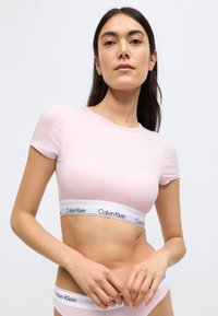 Ροζ αμάνικο crop top με κοντά μανίκια και λευκή ταινία με το λογότυπο «Calvin Klein». Μαλακό ύφασμα με ομαλή υφή.