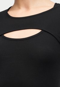 Κοντινό πλάνο ενός ατόμου που φοράει μαύρο πάνω μέρος με στρογγυλή λαιμόκοψη και οριζόντια διάτρηση πάνω από το στήθος.