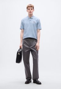 Ανοιχτό μπλε πουκάμισο πόλο με οριζόντιες ρίγες, γκρι πτυχωτό παντελόνι, μαύρη τσάντα και μαύρα παπούτσια. Απλός, μοντέρνος σχεδιασμός.