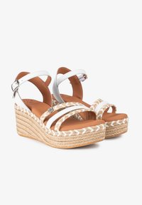 Sandalias de cuña de cuero blanco con suela de yute trenzado, correas cruzadas y cierre de hebilla. Plantilla de color marrón suave con acentos texturizados.