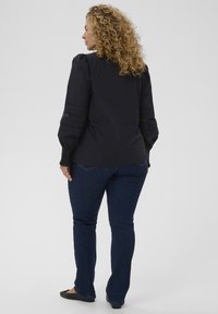 Blusa negra de mangas largas con detalle texturizado en las mangas, combinada con jeans azul oscuro. La blusa presenta un tejido suave y un diseño estructurado.