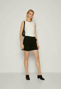 Black shorts and a white tank top, complemented by a small black handbag and black block-heeled shoes. Smooth fabric, tailored fit.
