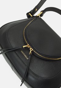 Sac à main en cuir noir avec une finition texturée, fermeture éclair dorée et accents en frange. Présente un design incurvé et un intérieur de marque.