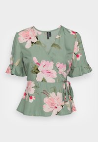 Blusa em tecido verde com estampado floral em rosa e branco, mangas curtas com volantes e um laço lateral para um ajuste regulável.